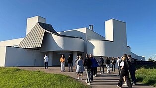 Menschen betreten vor blauem Himmel ein weißes Gebäude